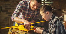 Father And Son Are Modeling A Toy Airplane In A Garage At Home.