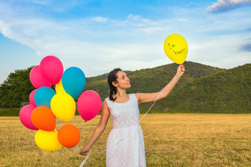 Cute young woman in white dress with balloons in her hands. The concept of freedom and joy. Balloon with text in the left hand