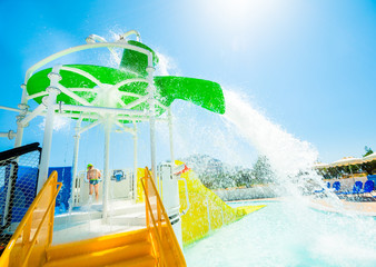 Children's water playgrounds and flip-flops with flowing, falling and splashing water. Moment pouring the bucket with water. In the background azure sky. The sun in the shot.