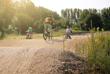 Mother And Two Daughters Riding Bike Together On A Bicycle Dirt Track In Bright Summer Light - Family Lifestyle Outdoor Activity Concept - Focus On Hill Tip In Foreground - Rider Blanked Out Blurry