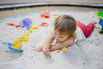 Wall Mural - Baby girl in sandbox playing with toys