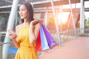 Beautiful women with shopping bags and smartphone enjoying in shopping standing outdoors of shopping mall, shopping concept