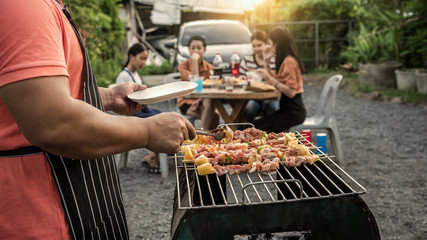 Wall Mural - BBQ party group of people at barbecue dinner friends having food together outdoor as summer with friendship asian person.