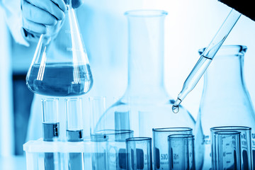 Wall Mural - hand of scientist holding flask with lab glassware and test tubes in chemical laboratory background,