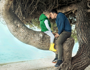 Happy childhood, father and son sit on a tree on a sunny day, fa