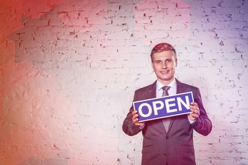 Portrait of smiling mature businessman holding open sign against brick wall at office