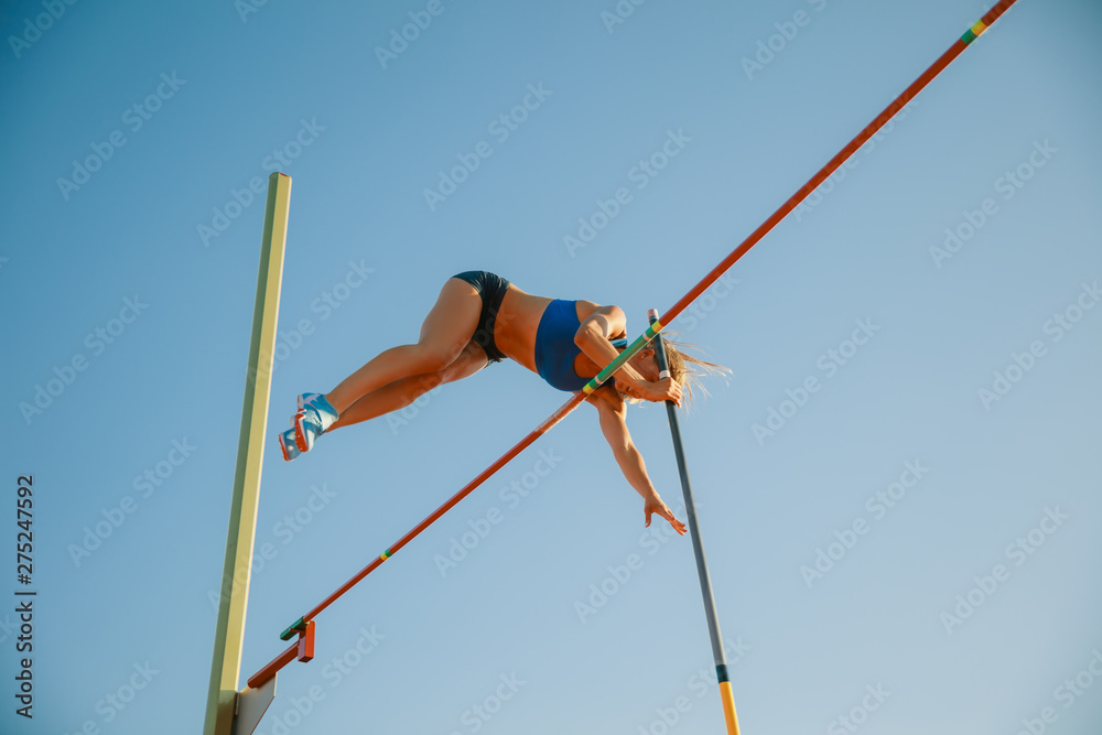 Professional female pole vaulter training at the stadium in sunny day. Fit female model practicing in high jumps outdoors. Concept of sport, activity, healthy lifestyle, action, movement, motion. - obrazy, fototapety, plakaty 