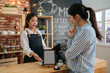 © PR Image Factory - digital tablet with blank screen in coffee shop. coffeehouse female worker hands showing gesture with menu on mobile pad in bar counter and talking to customer. lady client thinking while take order.
