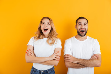 Sticker - Portrait of excited young couple man and woman in basic t-shirts wondering and looking upward with arms crossed