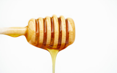 Honey dripping from wooden honey spoon on white background 