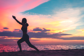 Sport Young woman silhouette practicing yoga on the sea beach at sunset