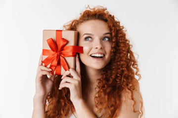 Excited young redhead curly girl isolated over white wall background holding surprise box gift.