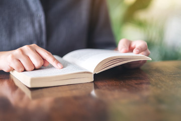 Closeup image of a woman pointing at a book while reading a vintage novel on wooden table