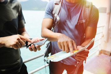 Two young travelers are planning a tour by looking at the map and searching on the smartphone.