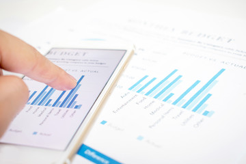 Poster - Close-up pictures of businessmen pointing to the smartphone screen showing some graphs. Modern white desk with financial documents.