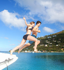 Young couple holds hands and jumps off a boat into the water. 