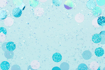 Festive frame of iridescent confetti and sparkles on pastel blue background. Trendy holiday backdrop. Flat lay, copy space.