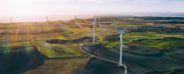 Aerial scenic view of renewable windmills turbines supplying cultivation area with eco power getting energy from wind blowing on vast area of agriculture meadows next to sea. Alternative electricity