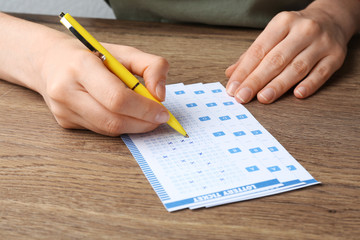 Woman filling out lottery tickets with pen on wooden table, closeup