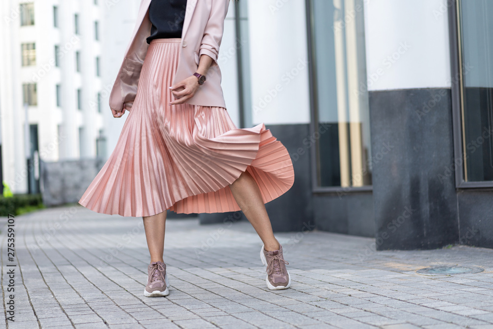 Pleated skirt coral color and sneakers. The girl is very dynamic posing on the street, the skirt is developing. - obrazy, fototapety, plakaty 