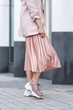 Model posing in a peach skirt, pleated, sneakers and jacket. Coral or pink color. On the street in the afternoon.