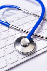 Wall Mural - Blue stethoscope on computer keyboard on white table background. Online medical information treatment technology concept, close up, macro, copy space