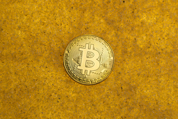 one bitcoin crypto coin on a shiny golden sand background with backlight, top view.