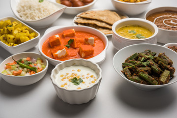 Canvas Print - Assorted Indian food like paneer butter masala, dal, roti, rice, sabji, gulab jamun and bound raita served in bowls over moody background, selective focus