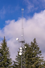 Communication tower with group of parabolic antennas against clouds on a blue sky