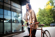 © NDABCREATIVITY - Young businesswoman standing on a city street with bicycle