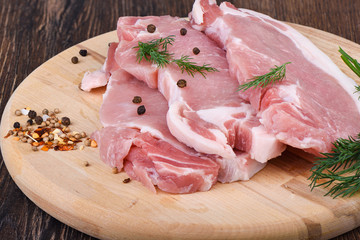 Pork steaks on a wooden cutting board with dill and spices. Raw pork meat for steaks.