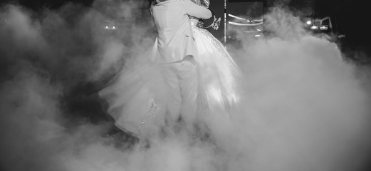 Wall Mural - First wedding dance of a couple. Beautiful lights and luxury dress. Bride and groom in love hugging.