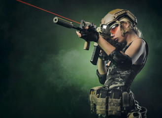 Wall Mural - the girl in military overalls airsoft posing with a gun in his hands on a dark background in the haze