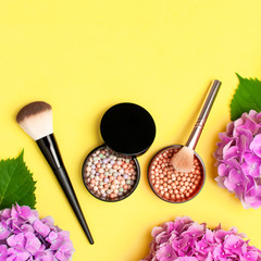 Set of decorative cosmetics makeup brushes, blush face balls, pink hydrangea flowers on yellow background top view Flat lay copy space. Beauty blogger concept. Fashion background. Makeup accessories