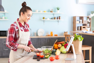 Beautiful woman preparing tasty vegetable salad in kitchen at home