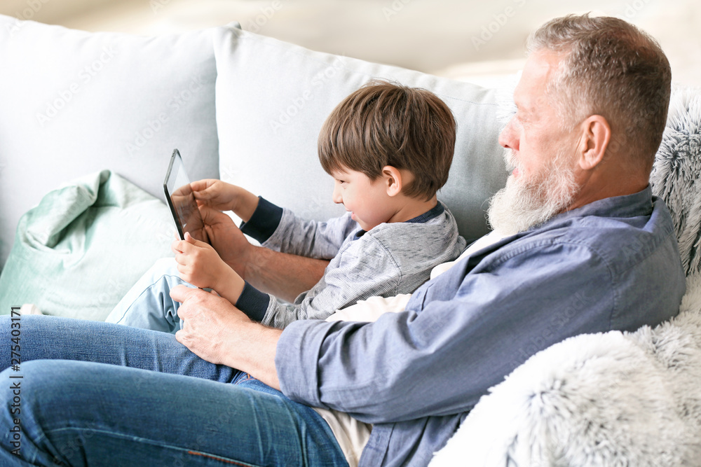Cute little boy and his grandfather with tablet computer at home
