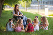 © Andrey - children hold a lesson with the teacher in the park on a green lawn.