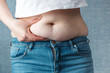 woman's hand holding excessive belly fat, overweight concept