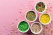 Cake sprinkles on pink background - Assorted colourful cake topping sprinkles in little white bowls on pink - top view