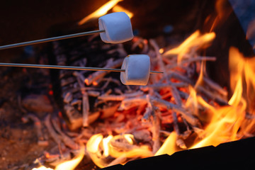 two marshmallows on the skewers roasting over the flames at the evening