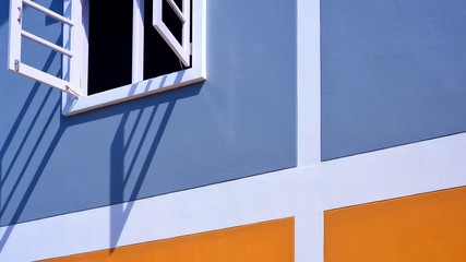 Low angle and side view of white wooden window in blue and orange painted wall decoration background with sunlight and shadow on surface, exterior architecture concept