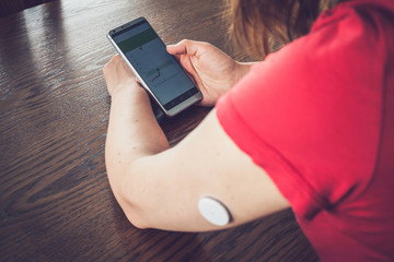 Wall Mural - Woman checking glucose level with a remote sensor and mobile phone, sensor checkup glucose levels without blood. Diabetes treatment. Focus on background.