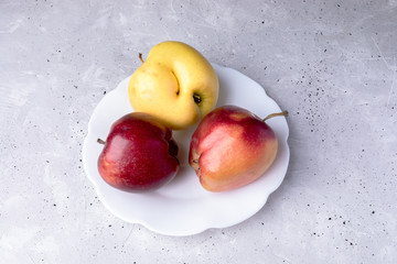 Wall Mural - Three ugly apples on white  figured plate on grey concrete background.