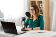 © Syda Productions - technology, mass media and people concept - woman in glasses with microphone and laptop computer talking and recording podcast at studio