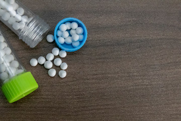 Scattered Homeopathic medicine bottles, globules in the cap on wood background.