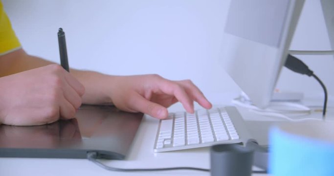 Closeup side view shoot of designer hands typing on the graphic touchpad working and editing indoors in the office