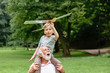 © Iryna - Little boy with airplane model and grandfather raising hands over green park on background enjoying life and nature. Portrait of happy grandfather giving grandson piggyback ride on his shoulders.