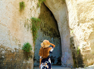 Back view of beautiful woman comes into the Ear of Dionysius (Orecchio di Dionisio) in Syracuse, Sicily, Italy