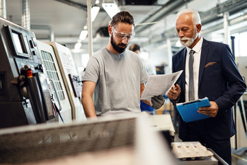 Young worker and senior manager analyzing paperwork in factory pant.