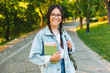 © Drobot Dean - Cute young student girl wearing eyeglasses walking outdoors in nature park holding books.